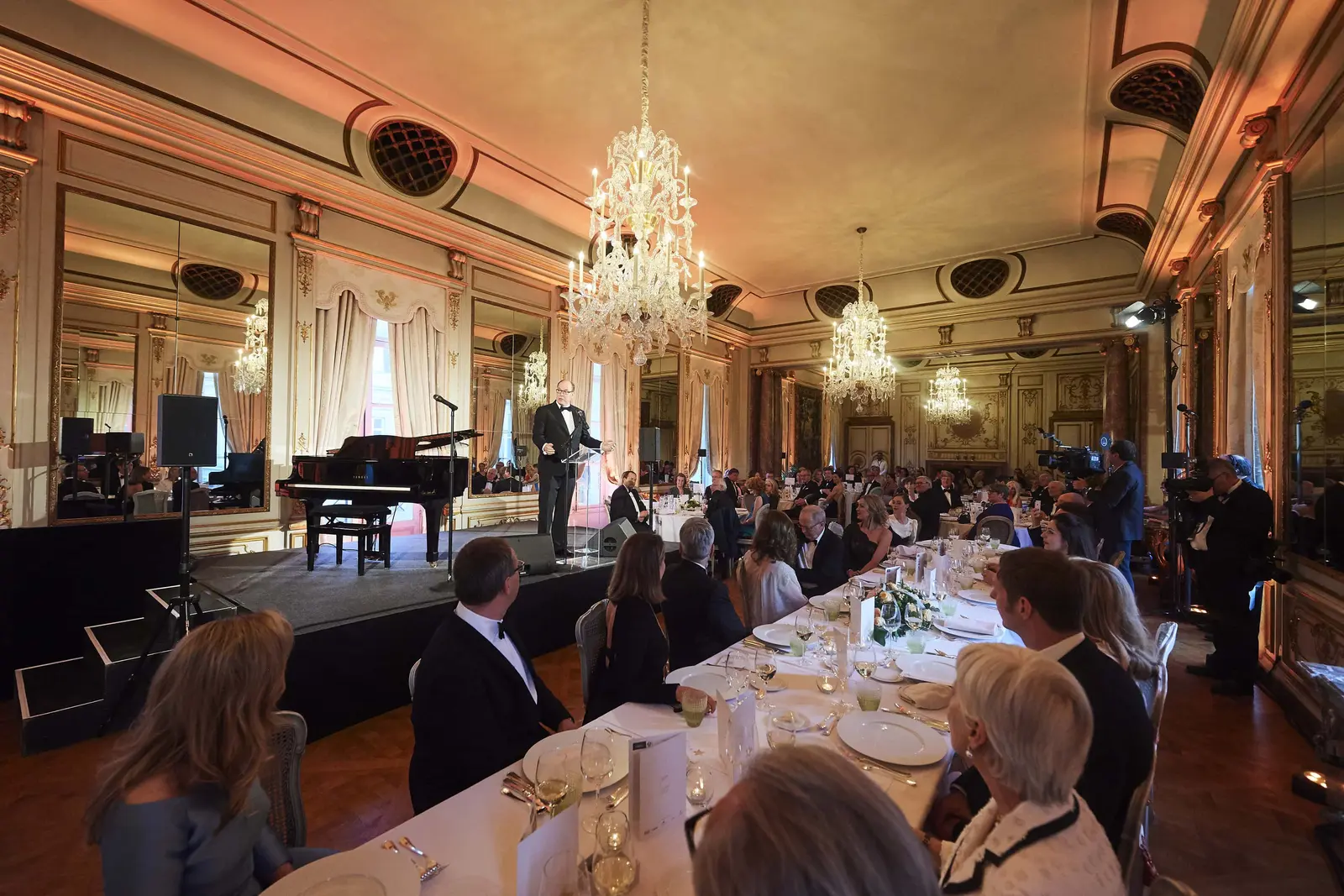Invités attablés pour le dîner dans un salon du palais d’Egmont à Bruxelles, un piano à queue sur une estrade