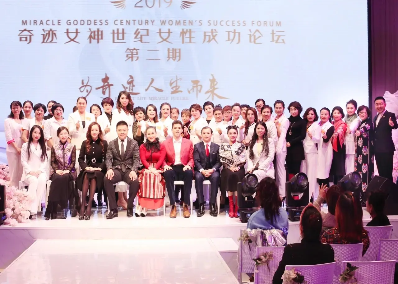 Photo de groupe des participants sur une scène, sous un écran affichant Miracle Goddess Century Women’s Success Forum 2019