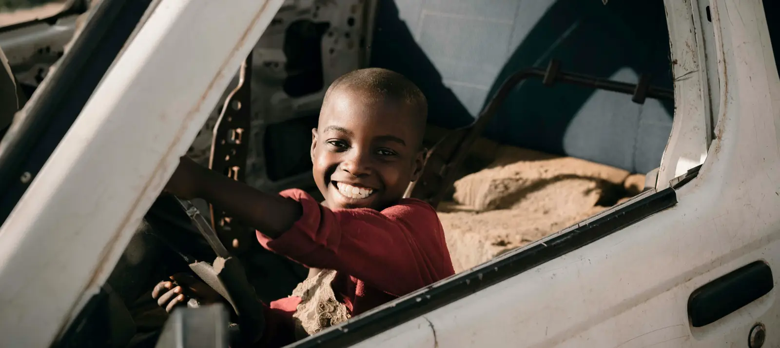 A smiling boy at the wheel of a damaged vehicle