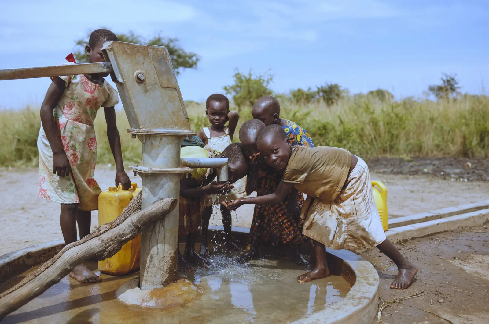 Children drinking and filling containers at a hand water pump