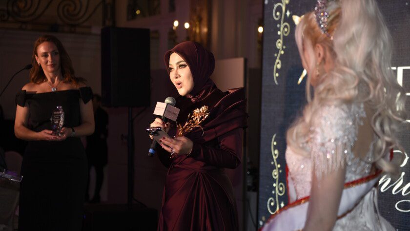 印尼巨星茜拉莉妮在2025戛纳电影节慈善晚宴演讲台照片：她身着晚礼服手持奖杯，身后是卡尔顿酒店大沙龙宴会厅的水晶吊灯与宾客。表情真挚，展现艺人与慈善家的双重身份。