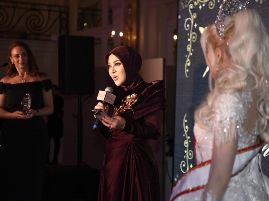 印尼巨星茜拉莉妮在2025戛纳电影节慈善晚宴演讲台照片：她身着晚礼服手持奖杯，身后是卡尔顿酒店大沙龙宴会厅的水晶吊灯与宾客。表情真挚，展现艺人与慈善家的双重身份。