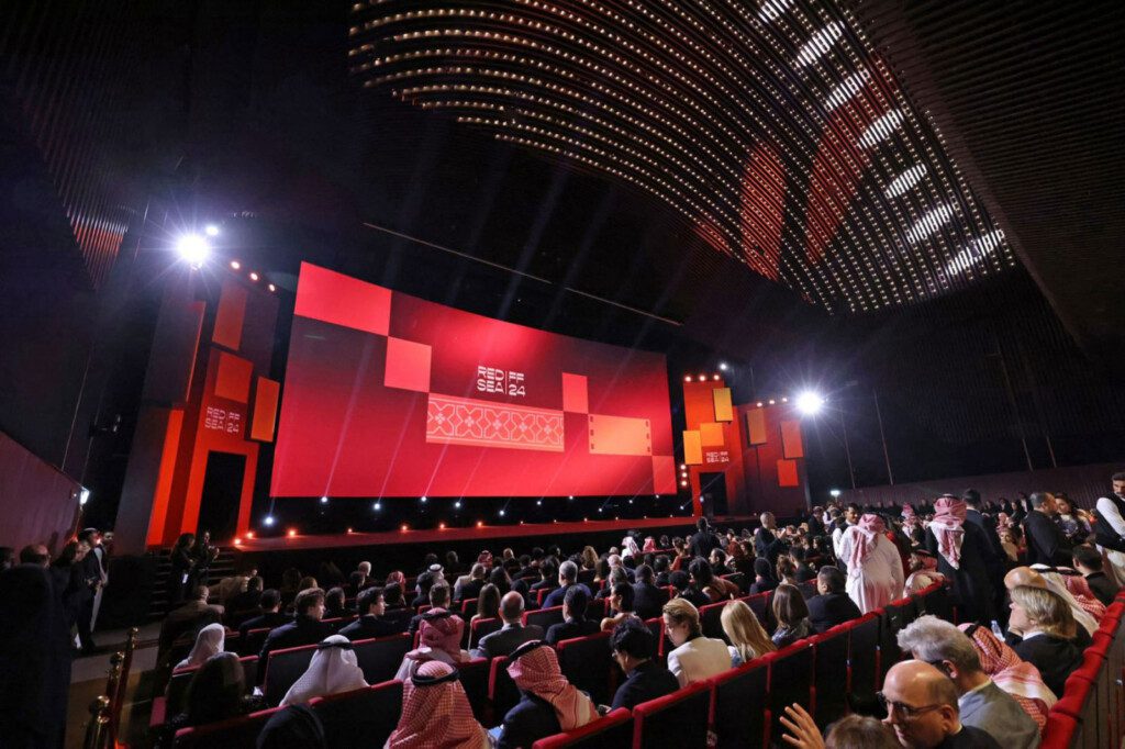 Audience perspective from seats inside a Red Sea Film Festival screening venue, with a large screen and ambient lighting.