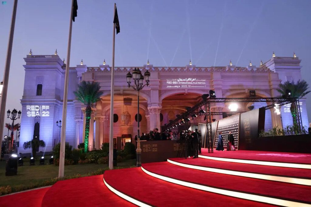 The Red Sea Film Festival building and red carpet under golden dusk lighting, with attendees and architectural details visible.